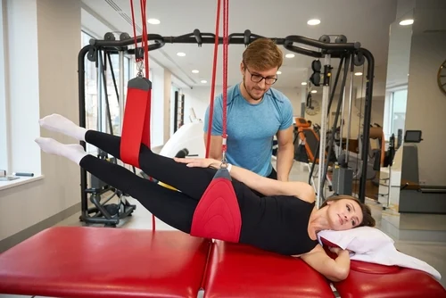 A young woman does a glute bridge on a yoga mat at home with her phone beside her