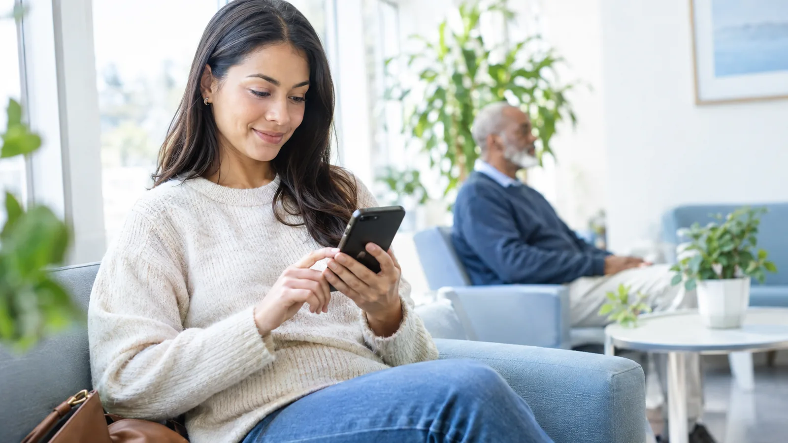 A patient completes a short questionnaire on a smartphone in a bright clinic waiting area
