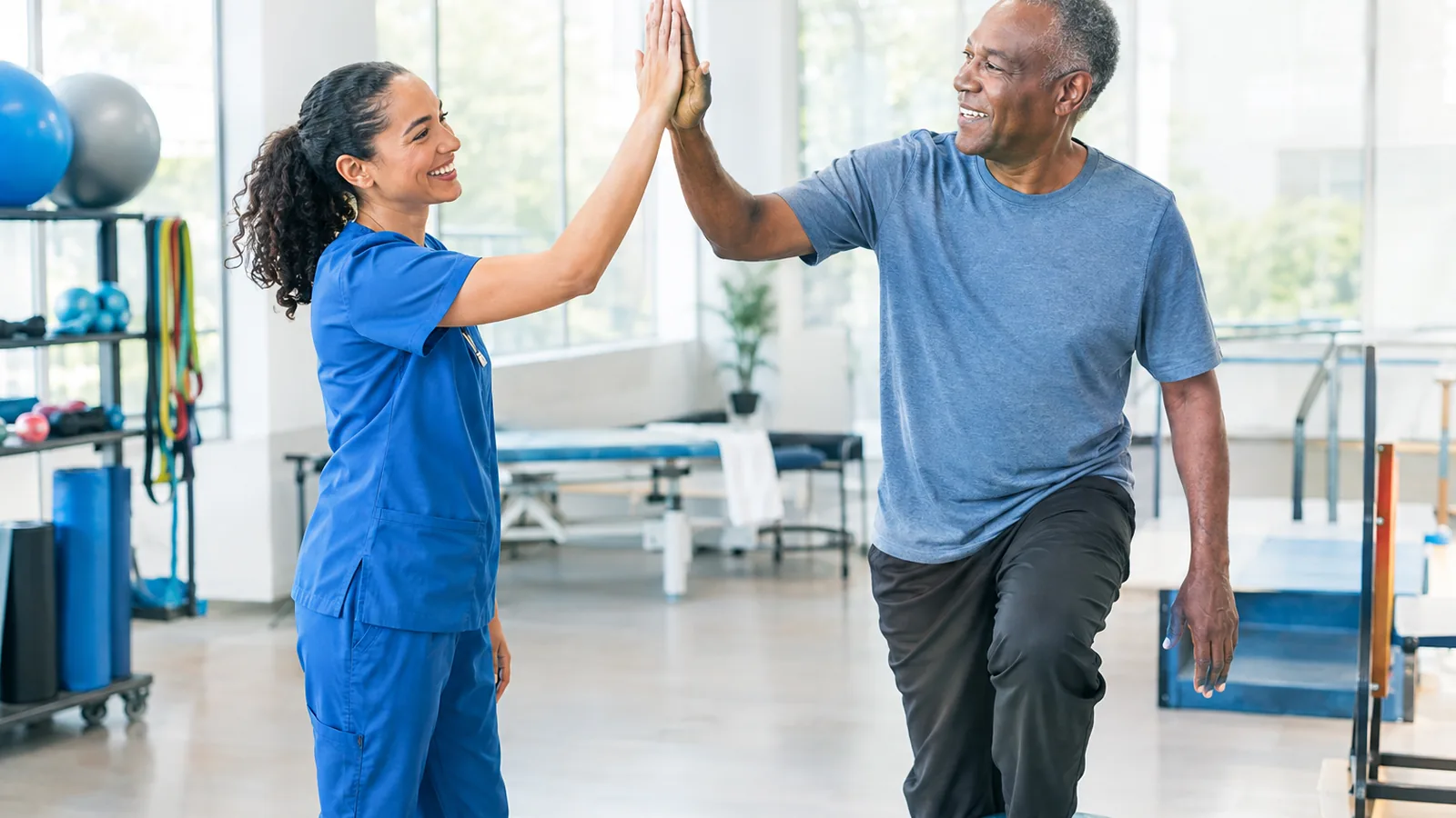 A physical therapist and a smiling patient high-five in a bright rehabilitation gym