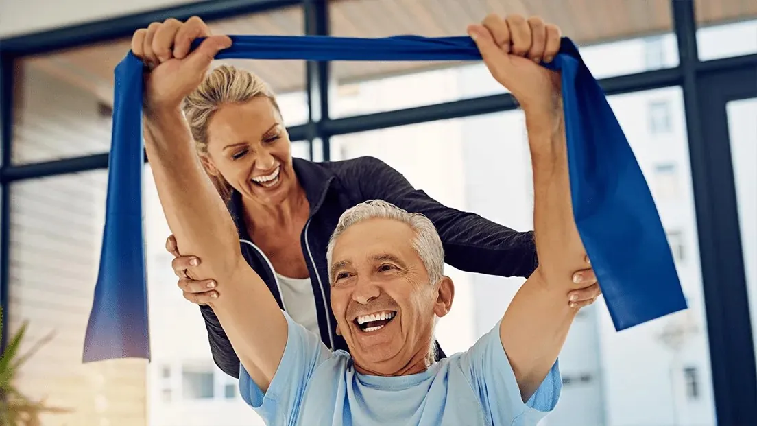 A physical therapist guides a smiling older patient through a resistance band exercise