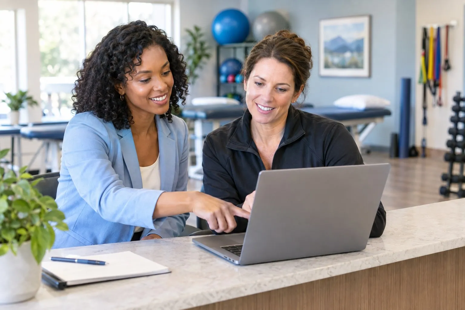A TheraPro onboarding specialist sets up a clinic owner's workspace on a laptop at the front desk